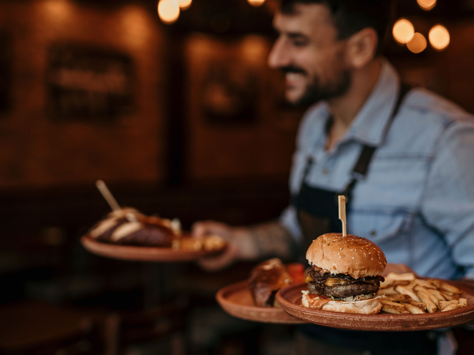 Smiling waiter holding tray with burger and fries